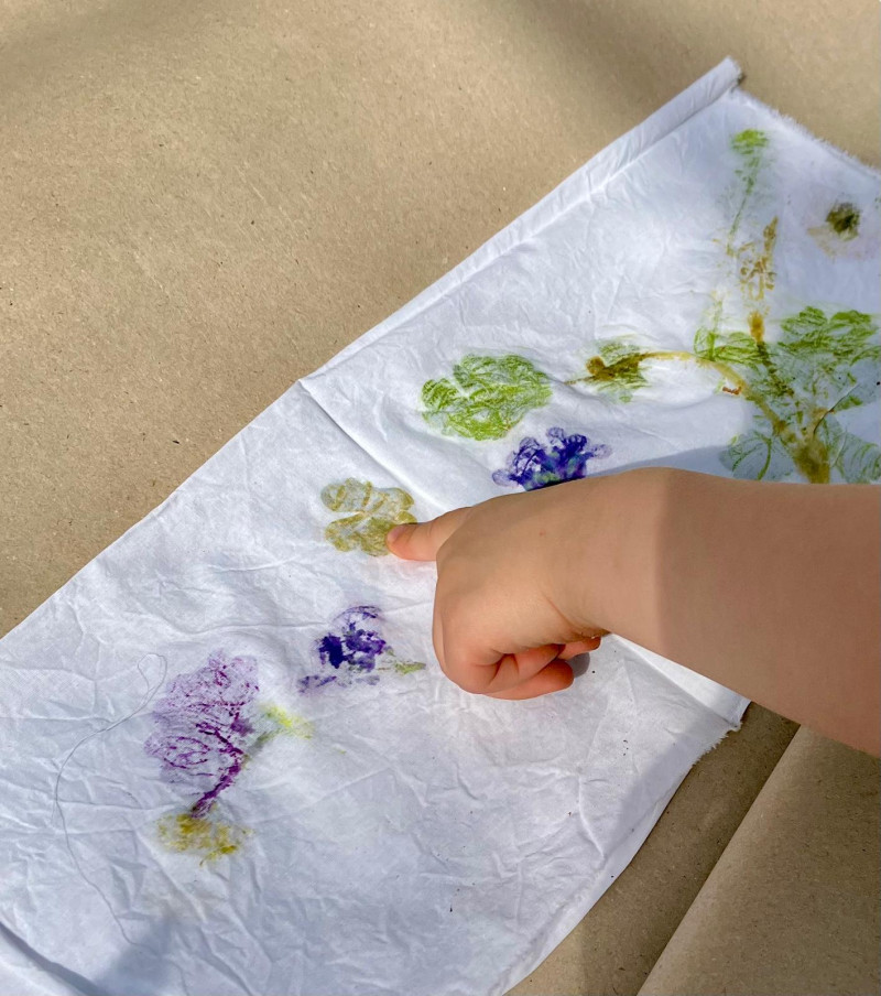 text: >
  Eine Kinderhand zeigt auf einen weißen
  Stoff, auf dem lila und grüne Blüten
  gedruckt wurden.
decorative: false
source: manual