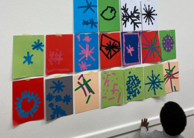 Bunte Papiercollagen mit verschiedenen Sternen- und Schneeflocken-Motiven an einer Wand, mit einem Kind im Vordergrund