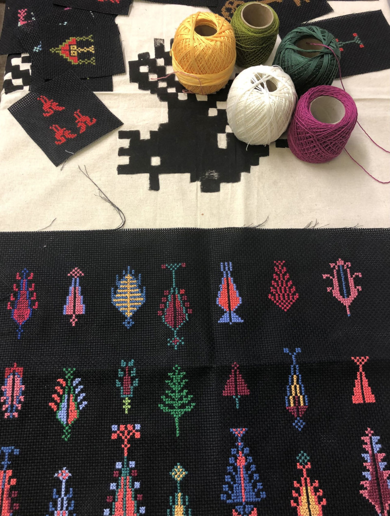 text: >
  Handgesticktes Tatreez-Projekt auf
  schwarzem Stoff mit traditionellen
  palästinensischen Motiven in bunten
  Farben und mehrere Wollgarne in
  verschiedenen Farbtönen daneben
decorative: false
source: reviewed