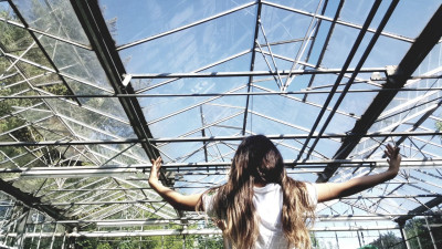 Person mit ausgebreiteten Armen steht in einem Glashaus und blickt zur transparenten Decke