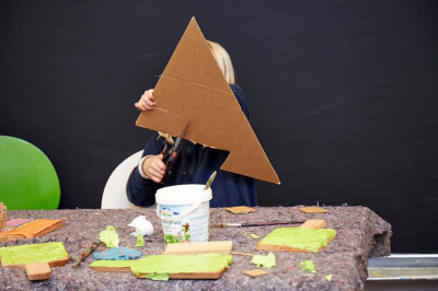 Kind bastelt mit Pappe und grüner Farbe an einem Tisch während eines Kreativworkshops