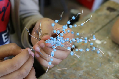 Zwei Hände halten glitzernde blaue Perlenketten mit silbernen Drähten