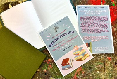 Flyer für einen kreativen Buchclub mit Informationen zu Terminen und Aktivitäten, liegt neben einem aufgeschlagenen Notizbuch