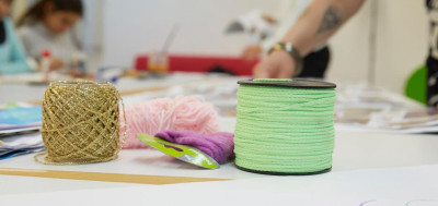 Bastelmaterialien mit goldener Kordel, bunter Wolle und grünem Garn auf einem Arbeitstisch